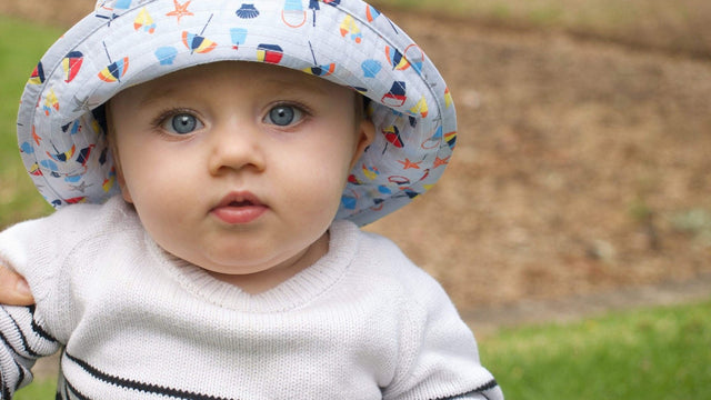 Baby in a printed sun hat with a chin toggle looking at the camera outdoors