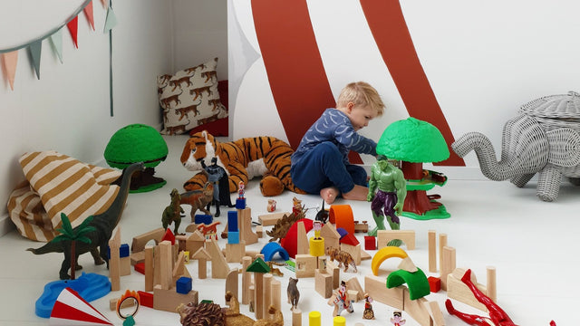 Toddler playing with blocks and toys spread across a playroom floor - the daily toy explosion good toy storage and playroom organization tames