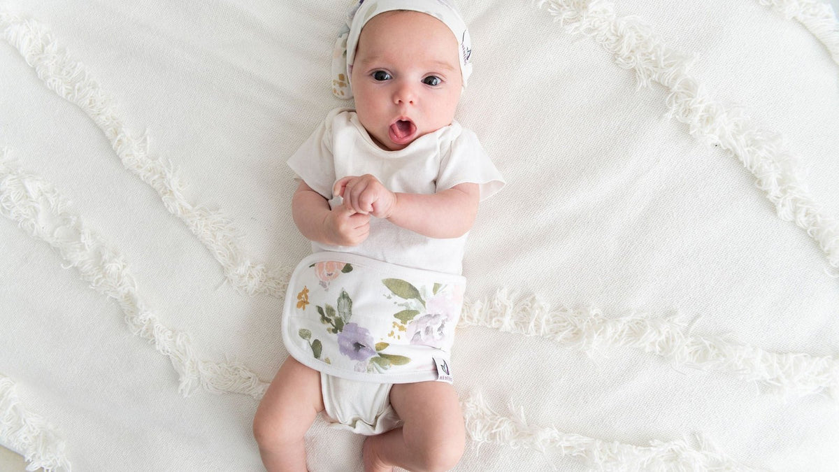 One-month-old newborn in a white outfit lying on a textured bedspread with arms raised