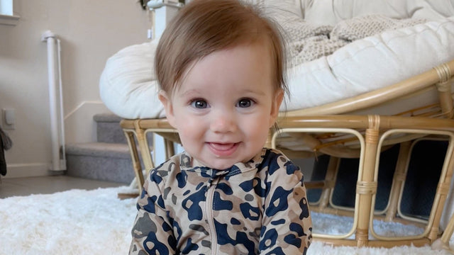 Smiling eleven-month-old baby sitting up on a playroom rug in a leopard-print romper