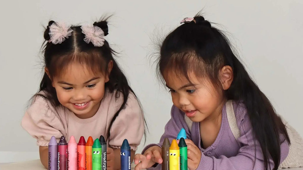 Young girl raising a chunky pencil over her drawing at a table