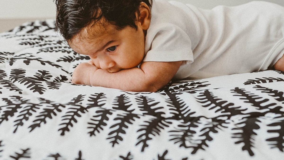 Baby resting on his forearms during tummy time on a black-and-white fern-print play mat