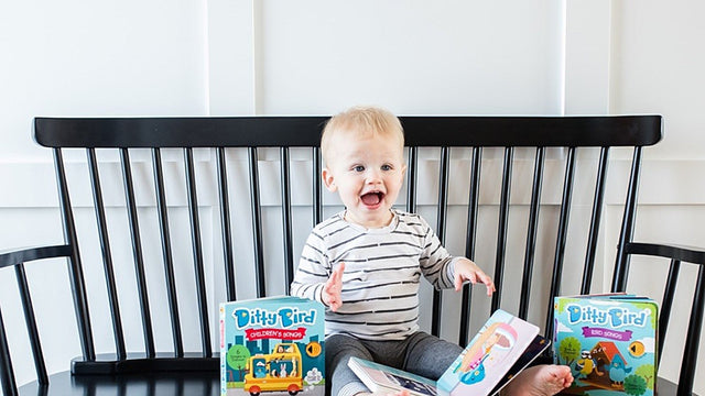 Laughing baby sitting on a black spindle bench surrounded by musical board books