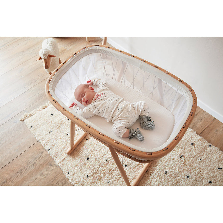 Newborn sleeping in a premium wooden bassinet on a nursery rug — the kind of curated baby gear parents register for