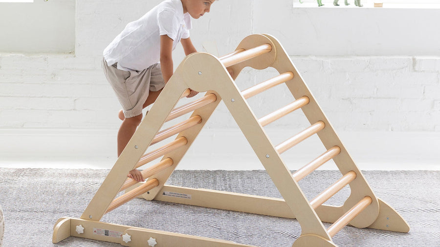 Young child climbing a natural birch Pikler triangle on a rug in a bright playroom