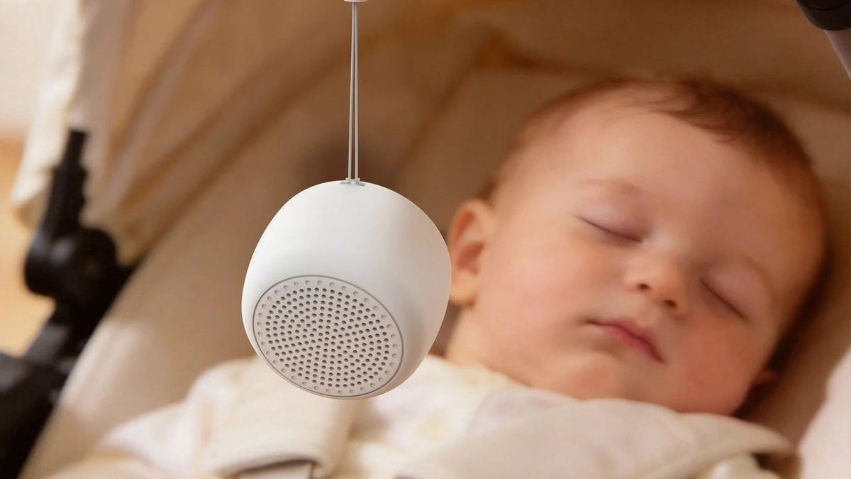 Baby asleep in a stroller with the Babelio Mini white noise machine hanging from the canopy