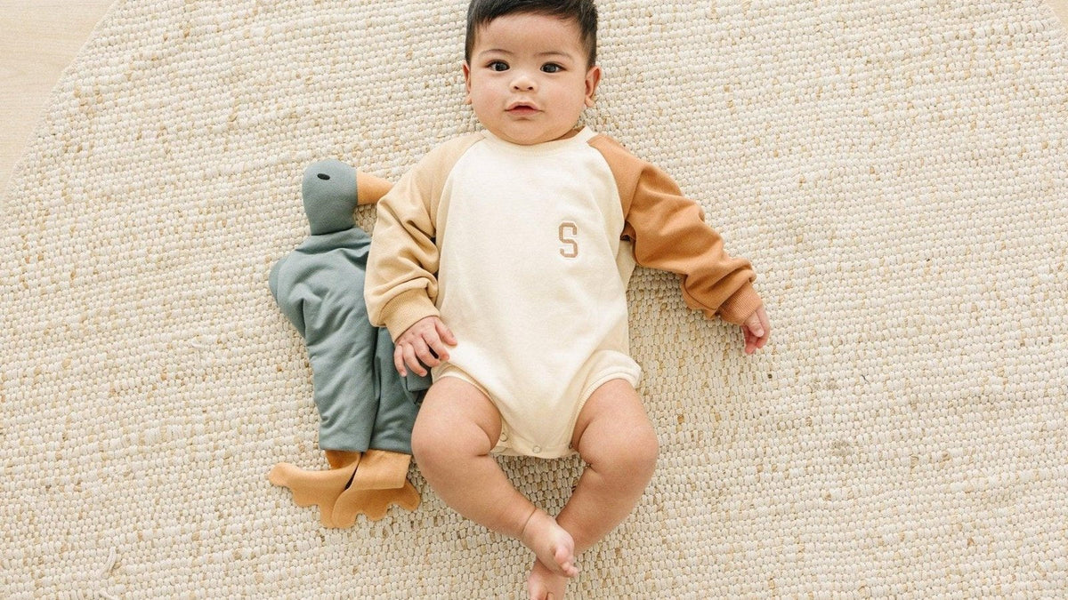 Wide-awake baby lying on a woven rug beside a duck lovey