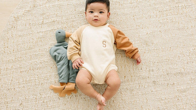 Wide-awake baby lying on a woven rug beside a duck lovey