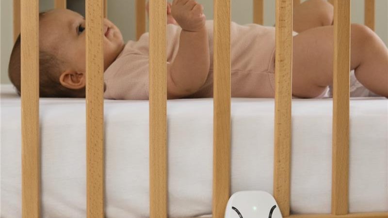Baby lying in a crib with the Babysense 7 non-WiFi breathing monitor control unit clipped to the crib frame