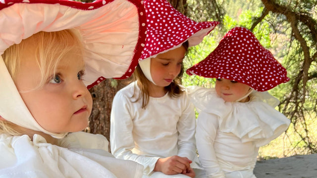 Three kids in Band of the Wild mushroom pajama costumes with red spotted hats under a tree