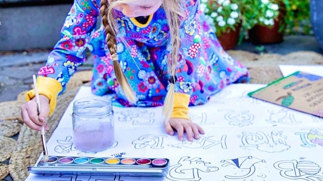 Girl kneeling outdoors painting a jumbo coloring poster with a Honeysticks watercolor set and brush