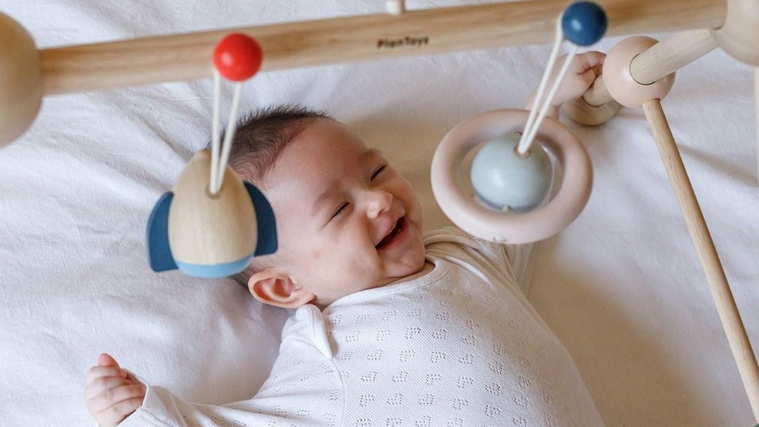 Smiling baby playing under a wooden activity gym