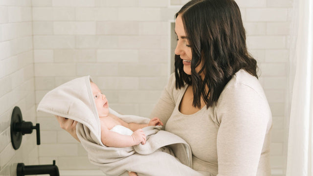 A parent lifting a newborn out of the bath wrapped in a hooded baby towel