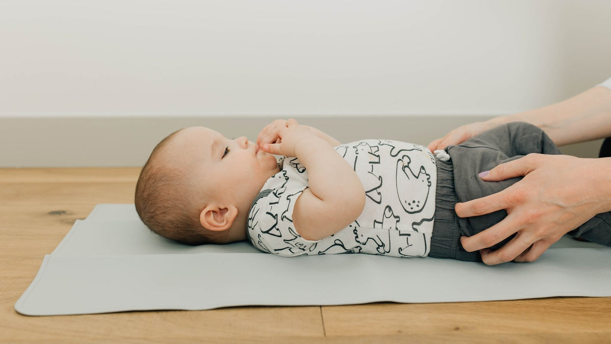 Baby lying on a wipe-clean vegan leather changing mat on a wood floor during a diaper change