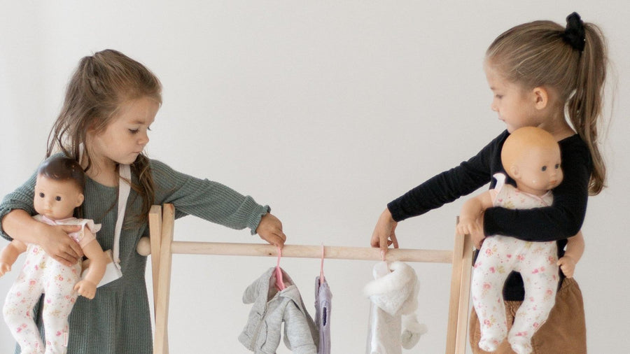 Two children playing pretend with baby dolls and a clothing rack