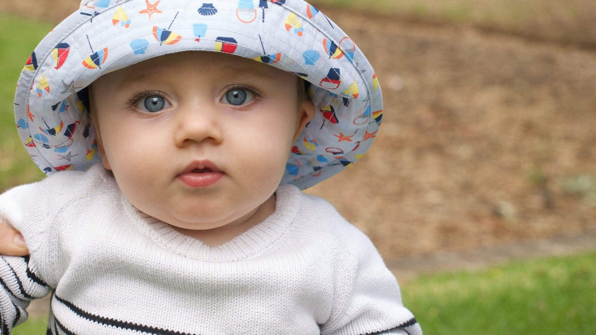 Baby in a printed sun hat with a chin toggle looking at the camera outdoors