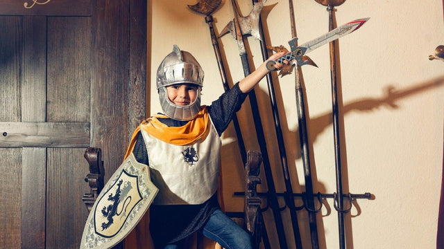 Child in a knight costume with helmet, shield and sword, striking a pose for Halloween dress-up