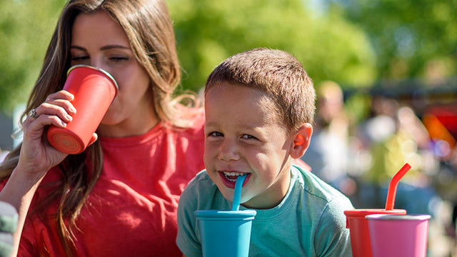 Two kids drinking from colorful Klean Kanteen straw cups at an outdoor picnic table