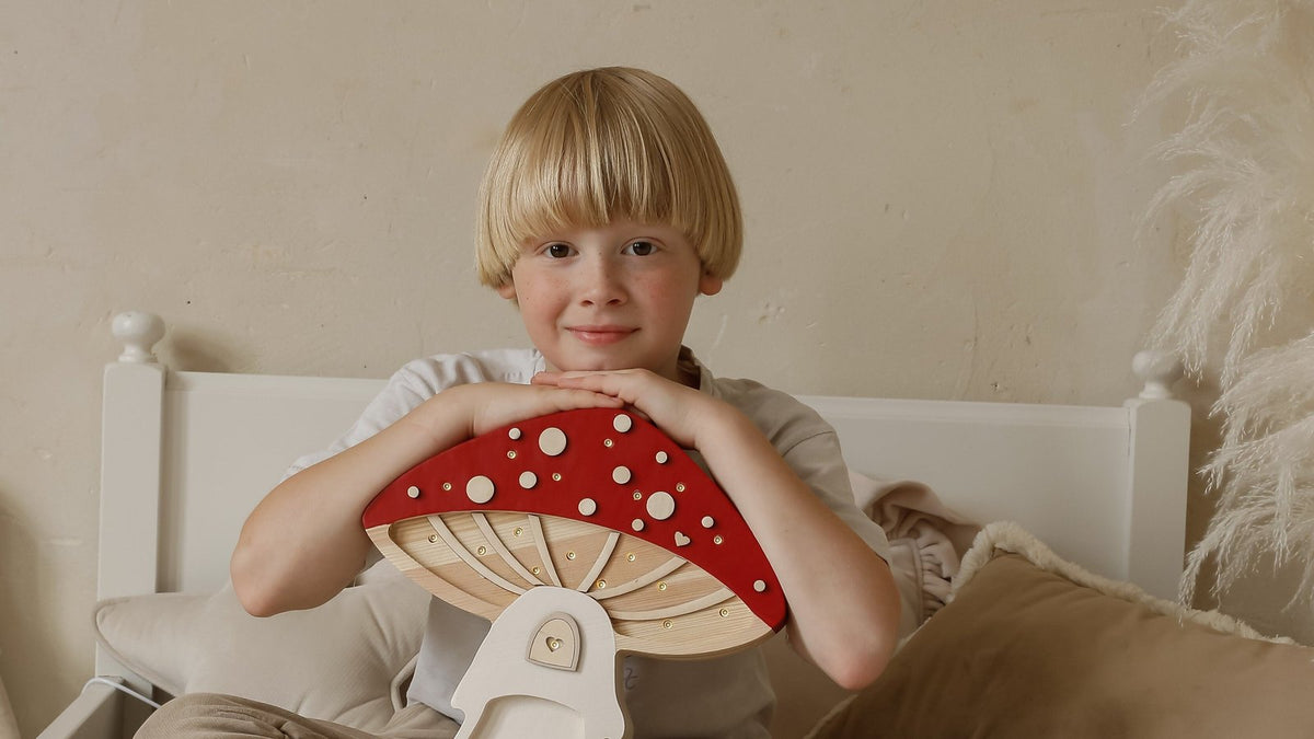 Boy on his bed hugging a red mushroom house kids night light by Little Lights