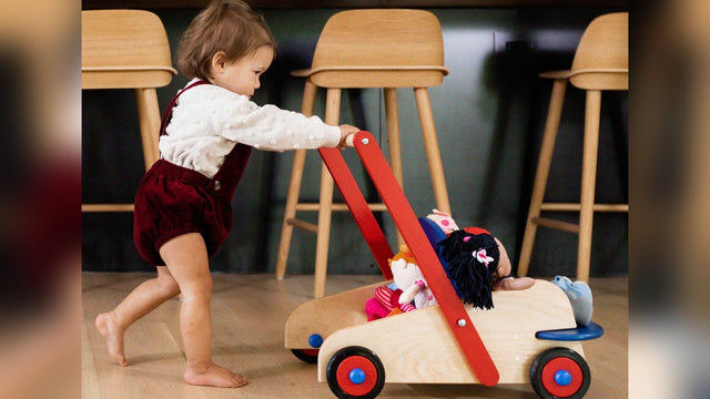 Toddler pushing a wooden push walker across a kitchen floor