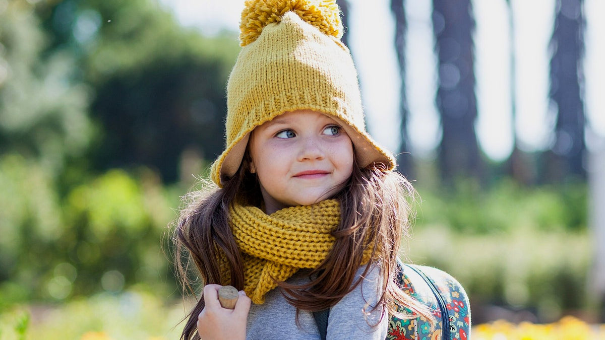 Toddler girl in a yellow knit hat wearing a small forest-animals backpack outdoors