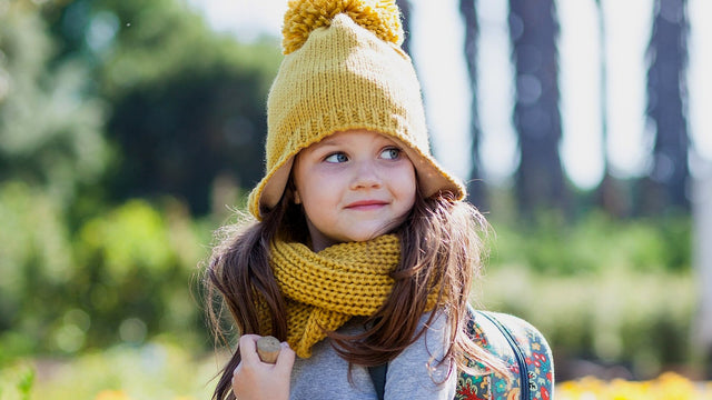 Toddler girl in a yellow knit hat wearing a small forest-animals backpack outdoors