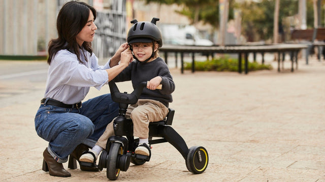 Parent fastening the buckle of a toddler bike helmet on a child sitting on a trike
