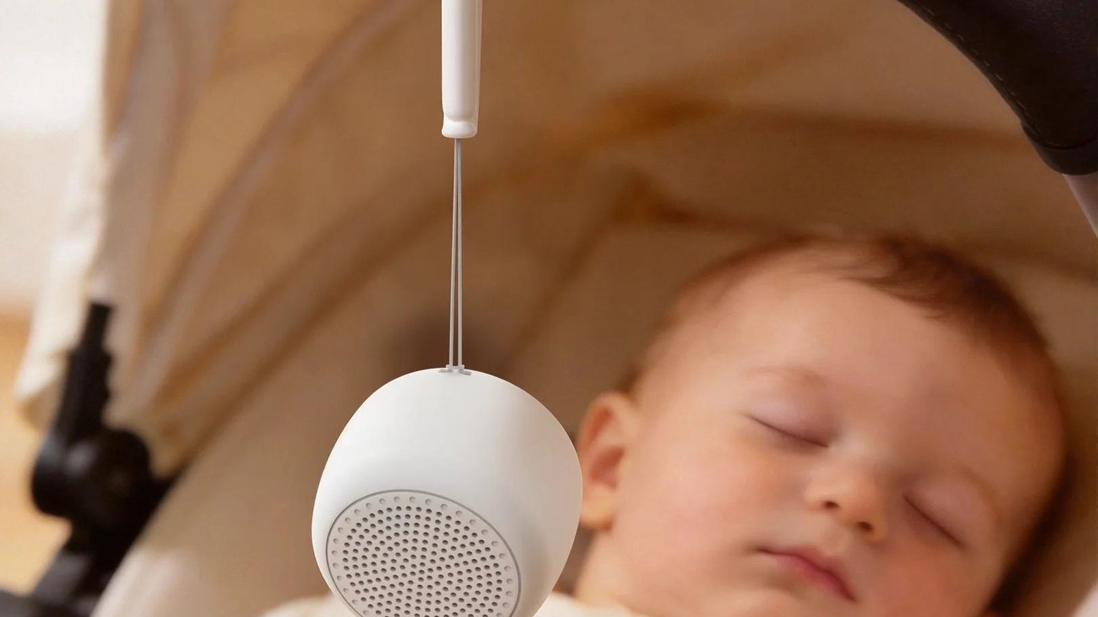 Baby sleeping in a stroller with a portable white noise machine hanging from the canopy