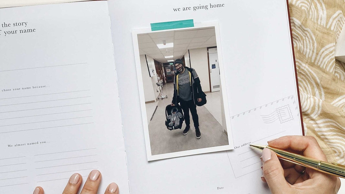 Hands writing in an open pregnancy journal beside a photo and a pen