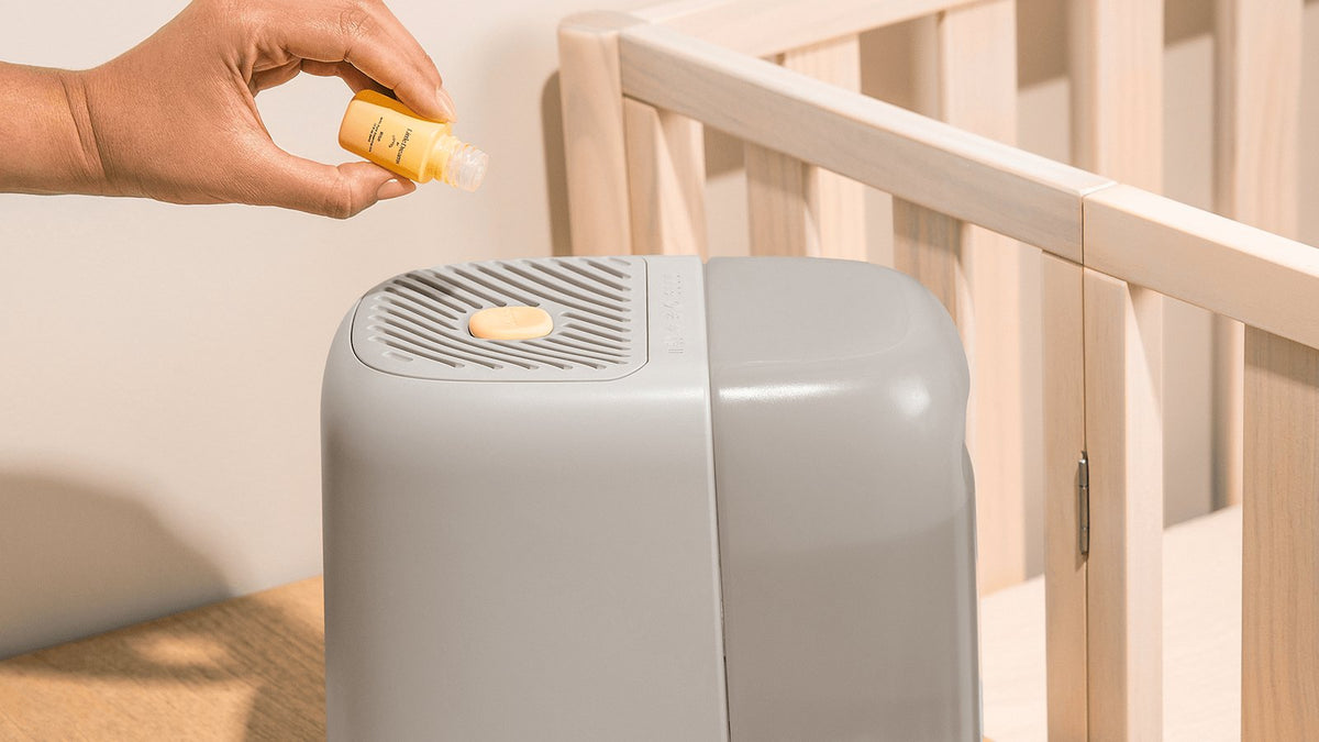 Parent adding a Little Dreams aroma drop to a Canopy nursery humidifier beside a wooden crib