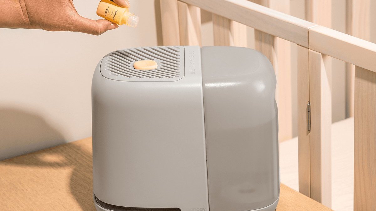 Parent adding a Little Dreams aroma to a Canopy nursery humidifier next to a crib