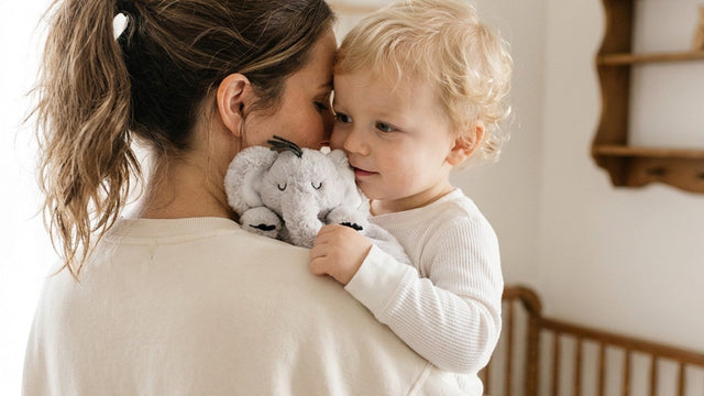 Toddler holding a plush doudou comfort blanket against a parent's shoulder in a nursery