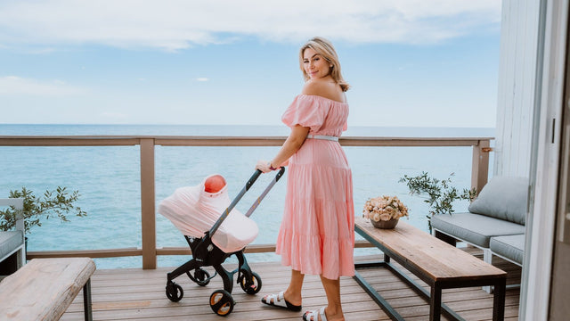 Mom on a seaside hotel balcony with her baby in a covered car-seat stroller on a family trip