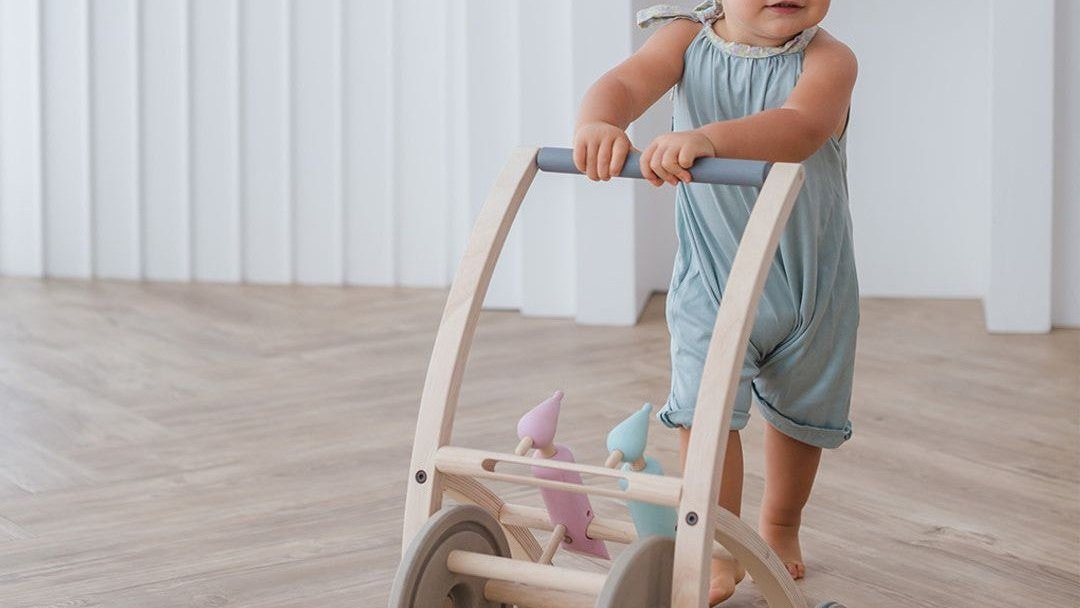 One-year-old girl walking with a wooden push toy