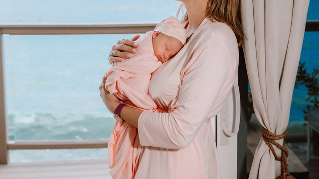 Mother holding her swaddled newborn at home by a window
