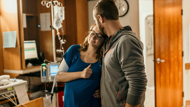 Expecting mother in a labor and delivery gown leaning on her partner in the hospital room — hospital bag checklist