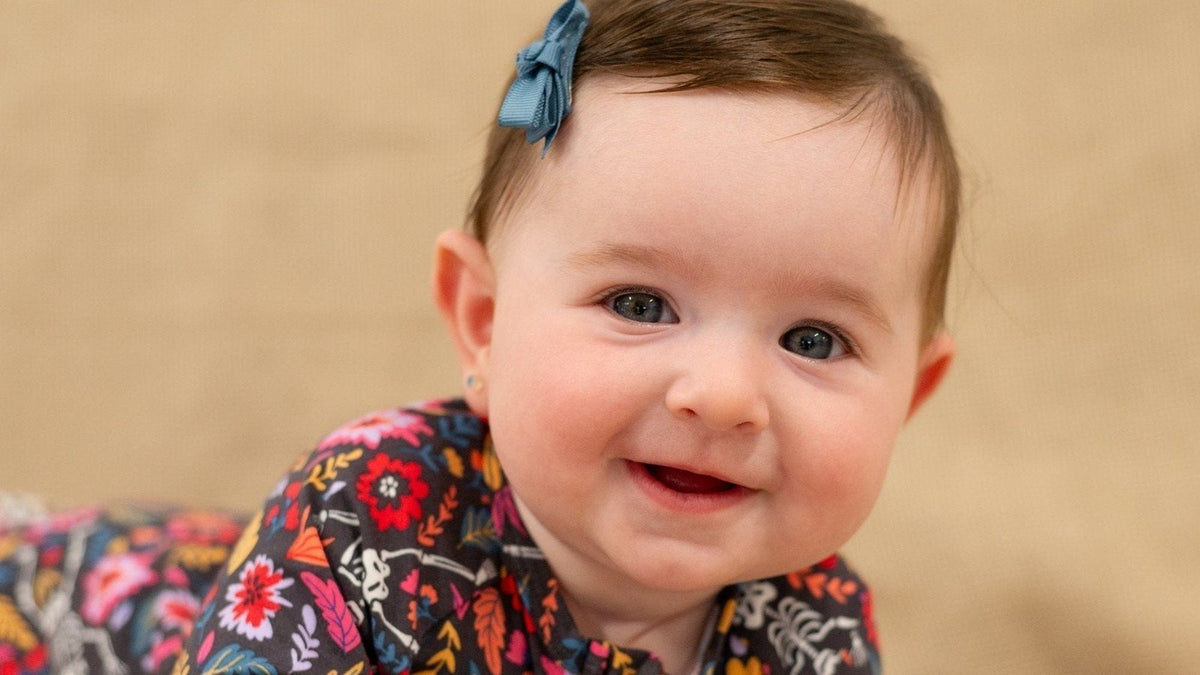 Smiling baby girl with a blue hair bow doing tummy time in a floral print outfit