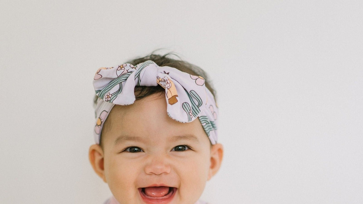 Laughing baby wearing a printed bow headband against a soft gray backdrop