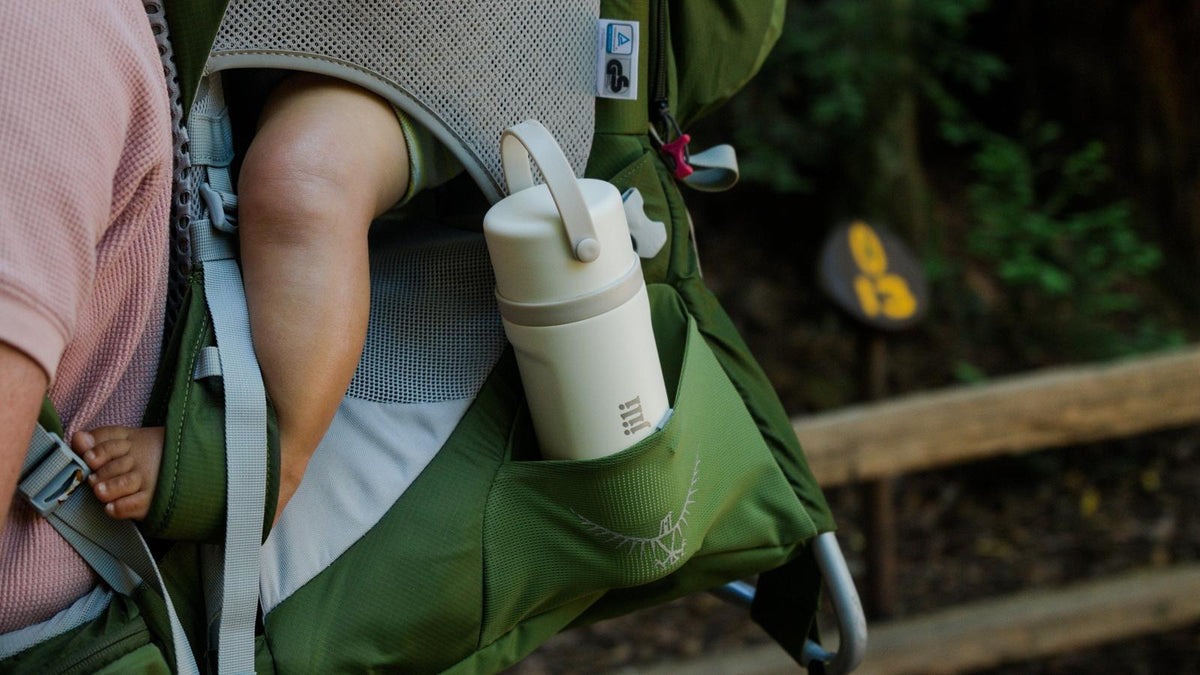 Jili all-in-one insulated baby bottle tucked in a hiking carrier pocket next to a baby's foot on a trail