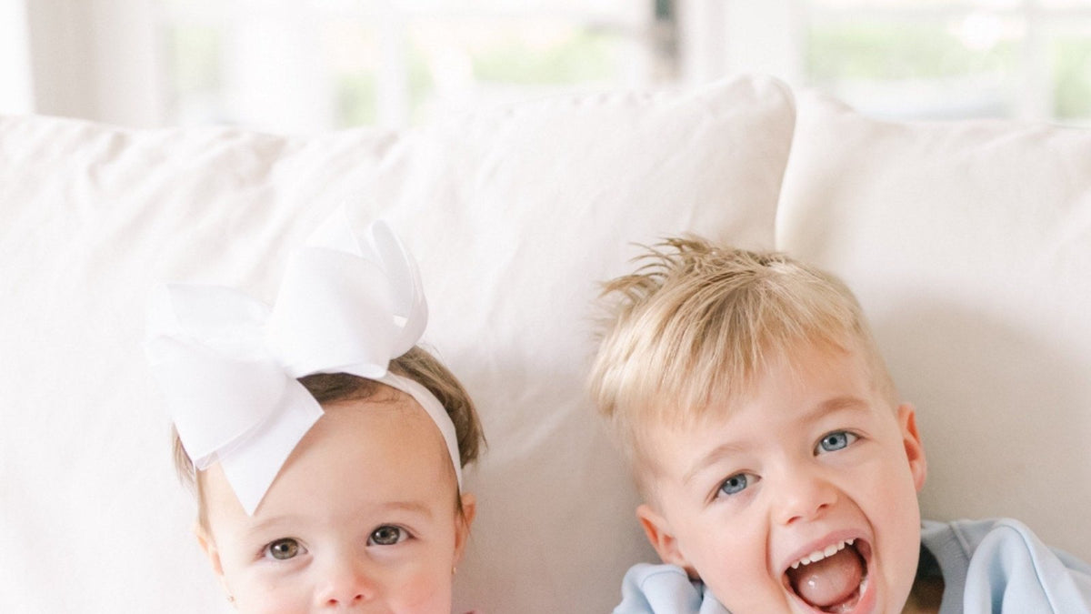 Toddler girl wearing a white bow headband next to her brother on a sofa - kids headbands and hair accessories