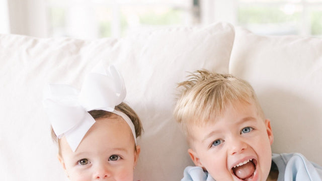 Toddler girl wearing a white bow headband next to her brother on a sofa - kids headbands and hair accessories