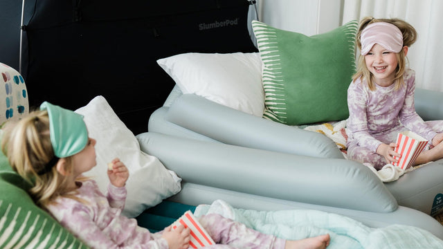 Two kids in pajamas and sleep masks having a sleepover on SlumberTot inflatable beds