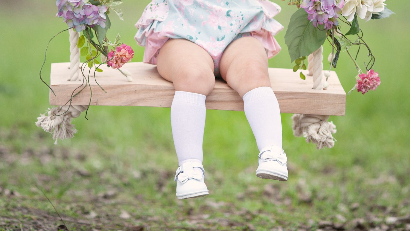 Baby on a flower swing wearing white L'Amour leather Mary Janes and knee socks