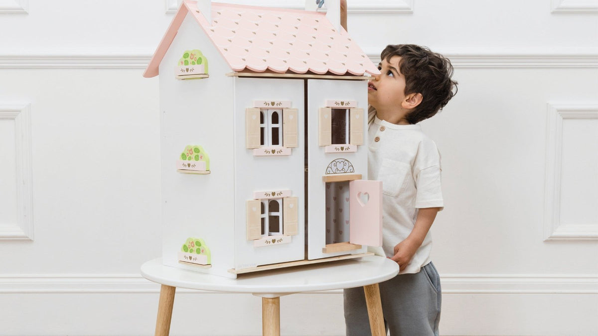 Little boy peeking into the Le Toy Van Rose Heart wooden dolls house on a play table
