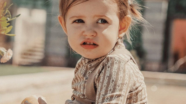 Toddler in a Lovely Littles printed top and knit overall outdoors