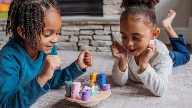 Two young siblings lying on the playroom floor playing a wooden stacking game together