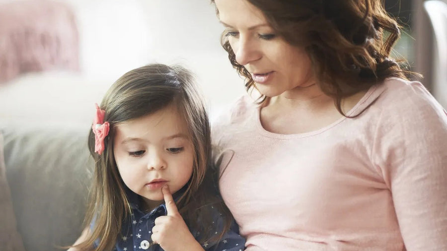 Mother and her young daughter sitting close together on a sofa at home, reading a picture book