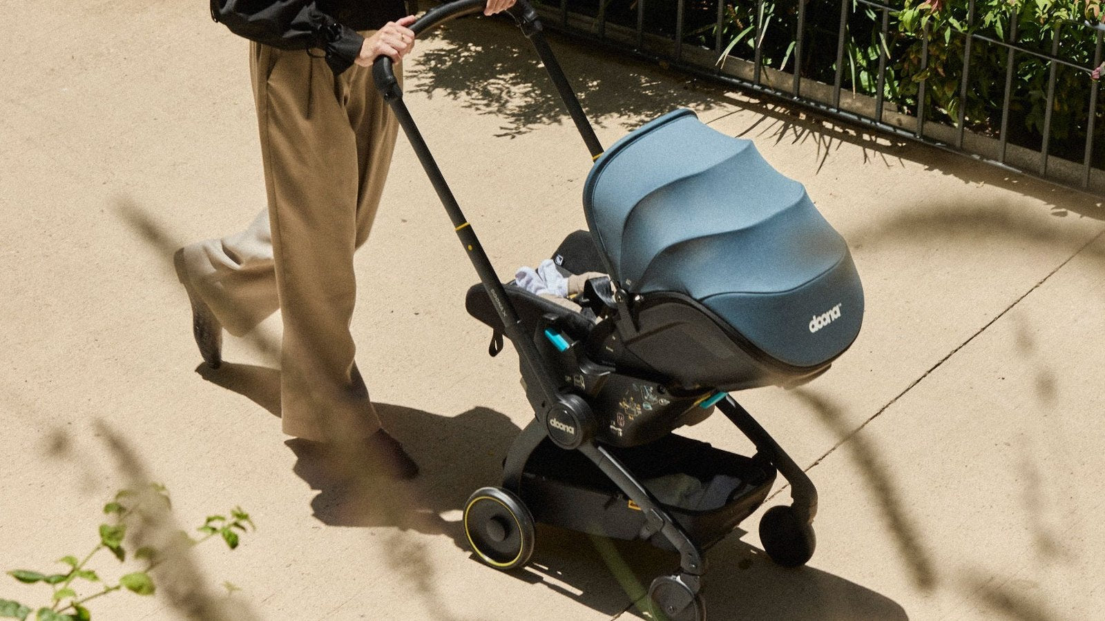 Parent walking a baby along a sunny path in a Doona infant car seat rolled out in stroller mode, canopy up