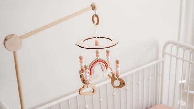 Wooden crib mobile on a rail-mounted arm above a bare crib with only a fitted sheet