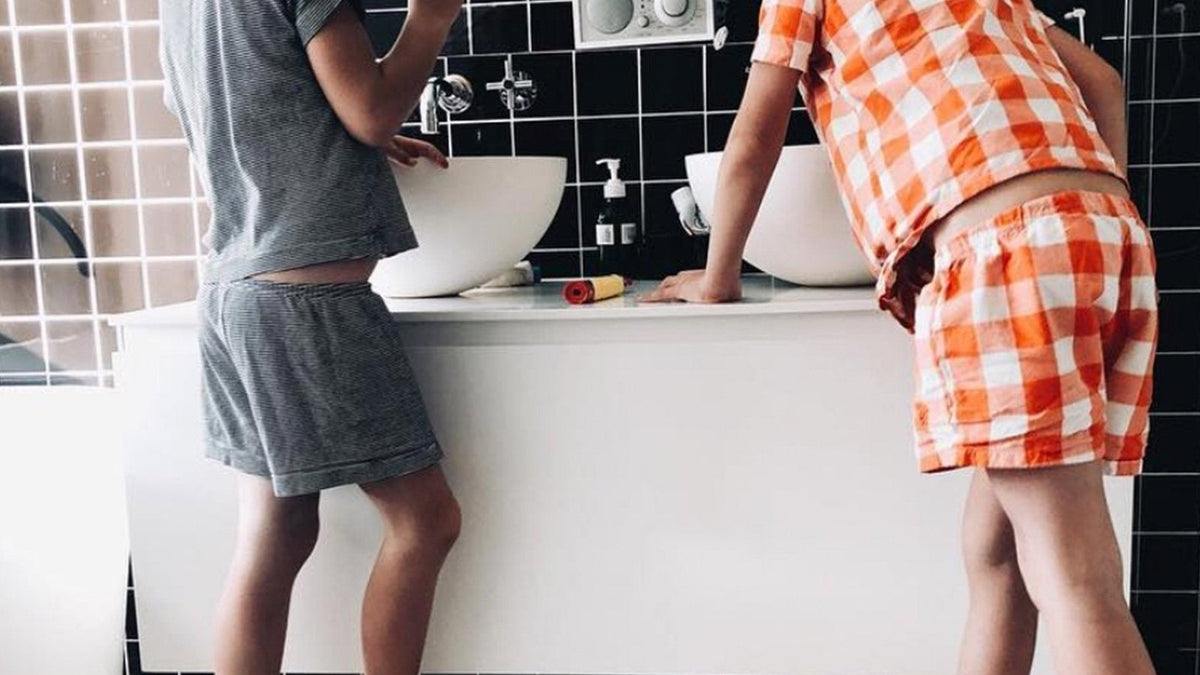 Two siblings in pajamas standing on step stools at a bathroom sink